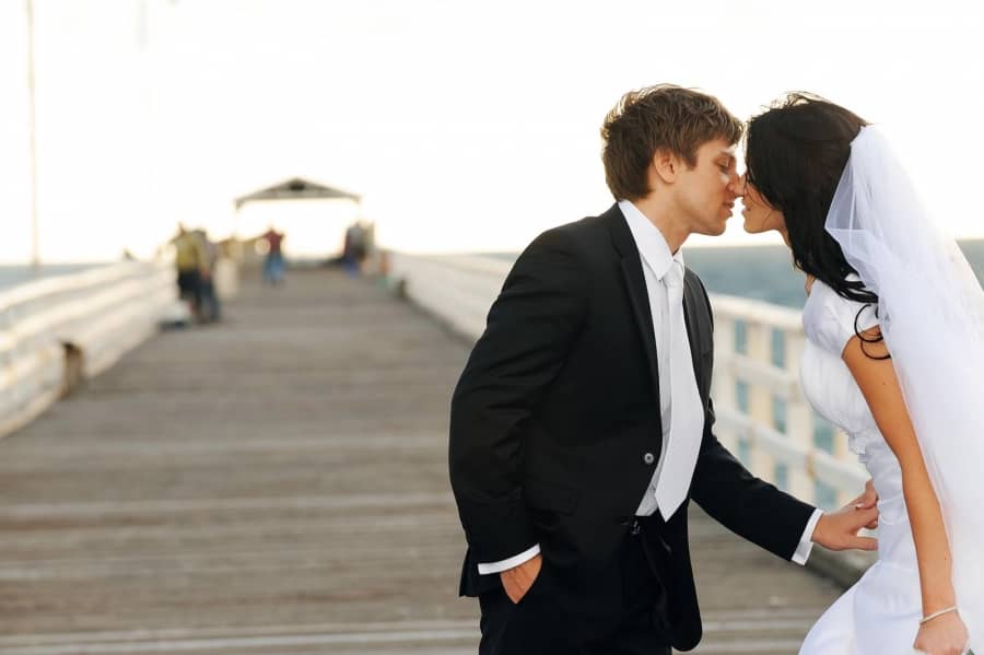 Newlyweds share intimate moment on pier at sunset, evoking romance and connection.